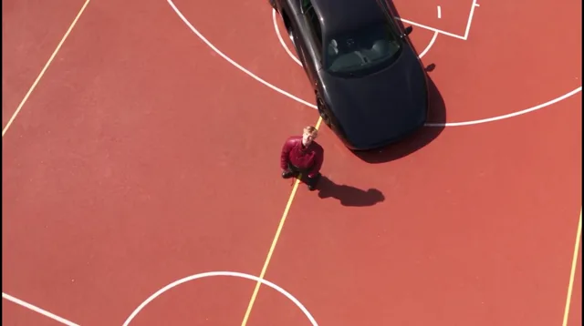 Drone overhead: from high above the red court, looking straight down on him and the black car, then lower and closer