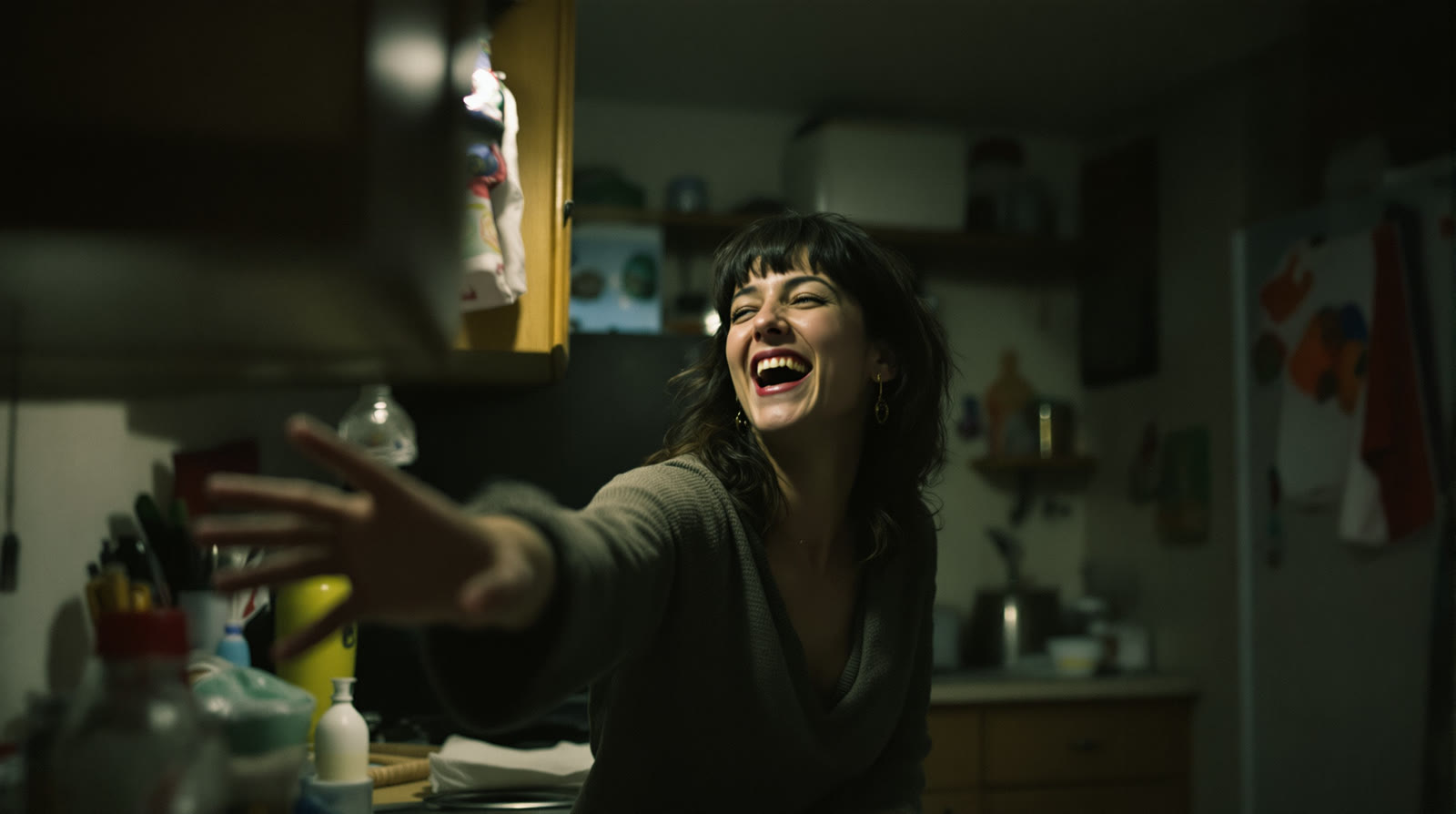 Example made with Flux Ultra: A candid unposed photograph in a cluttered home kitchen at night, shot on 35mm film with available light only: someone caught mid-laugh reaching…