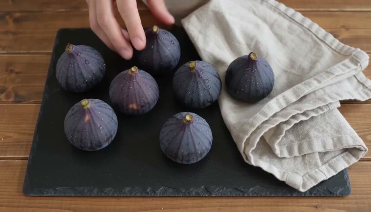 Example made with Seedance 2.0 Fast: Overhead: two hands arrange ripe figs and a linen cloth on a slate board, then a quick rack focus to a knife splitting one open, the flesh…
